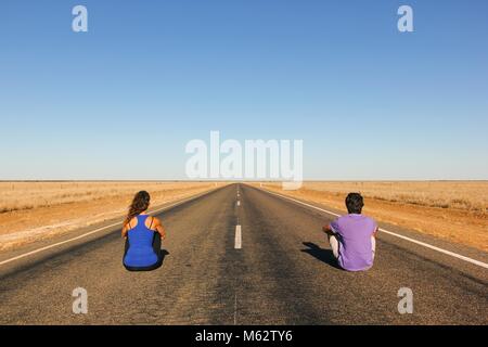 Coppia giovane da dietro seduti su un infinito vuoto dritta strada in mezzo al nulla nell'Outback australiano. Backpackers, concetto visionario Foto Stock