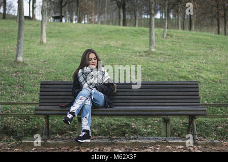 Giovane donna seduta su una panchina nel parco guardando verso il basso nello spazio accanto a lei. Manca il concetto di qualcuno. Solitudine e depressione Foto Stock