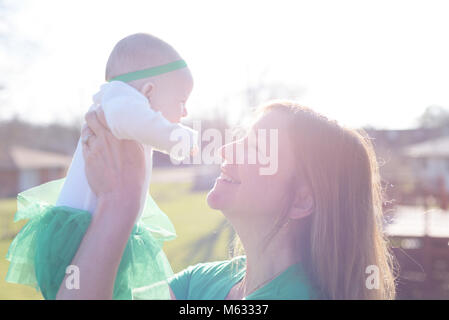 Donna che mantiene baby fino all'esterno in condizioni di luce solare intensa - sovraesposte per effetto Foto Stock