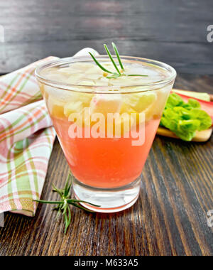La limonata con il rabarbaro e il rosmarino in un bicchiere, steli e una foglia di un vegetale, igienico su un asse di legno sfondo Foto Stock