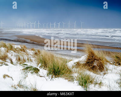 Marske dal Sea North Yorkshire Regno Unito 28 Febbraio 2018 UK Meteo. Continuando neve con un forte vento da est prendere per condizioni di freddo su una spiaggia deserta con neve in cima alla scogliera e una vista verso il Redcar per centrali eoliche offshore, nuvole nere all'orizzonte portare ulteriori la neve cade ancora a venire. Credito: Pietro Giordano NE/Alamy Live News Foto Stock