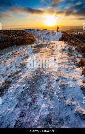 Flintshire, Wales, Regno Unito meteo: La Bestia forma est continua a devastare in molte aree nel Regno Unito con la neve e il gelo. Una mattina presto hill walker prendendo in sunrise su un percorso che segue il contorno della età del ferro Hill Fort di Moel y Gaer su Halkyn Mountain all'alba alle temperature di congelamento Foto Stock