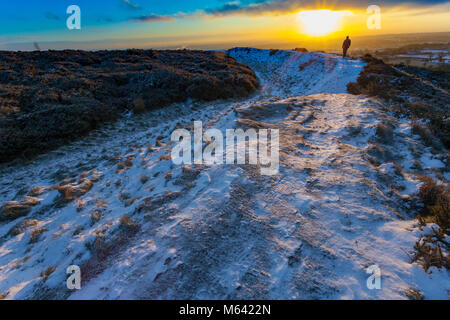 Flintshire, Wales, Regno Unito meteo: La Bestia forma est continua a devastare in molte aree nel Regno Unito con la neve e il gelo. Una mattina presto hill walker prendendo in sunrise su un percorso che segue il contorno della età del ferro Hill Fort di Moel y Gaer su Halkyn Mountain all'alba alle temperature di congelamento Foto Stock