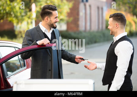 Sorridente giovane imprenditore in piedi accanto a AUTO dando la chiave di servizio Foto Stock