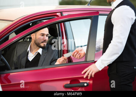 Servizio dando ricevuta al giovane imprenditore maschio seduta all'interno auto rossa Foto Stock