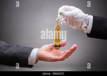 Close-up di receptionist dando Hotel Key al Cliente su sfondo grigio Foto Stock