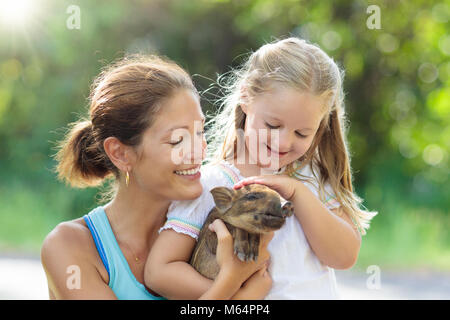 Bambini a giocare con gli animali della fattoria. Bambino alimentazione di animale domestico. Giovane madre e bambina tenendo il cinghiale baby al giardino zoologico. Kid giocando con newbo Foto Stock