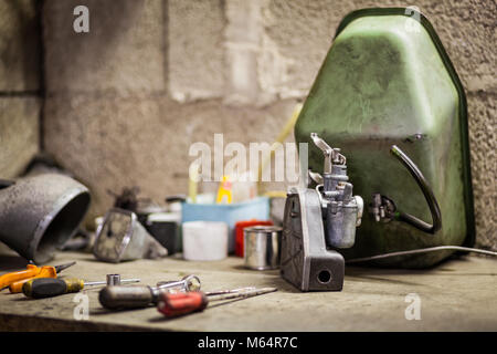 Piccolo carburatore con filtro aria e il serbatoio del combustibile del vecchio italiano moto scooter su un banco di lavoro con più parti e alcuni strumenti Foto Stock