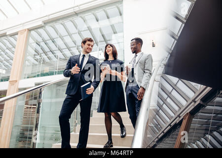 Tre multirazziale business persone che camminano giù su scale con tavoletta digitale Foto Stock