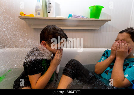 Twin fratelli caucasici giocare nella loro acqua riempito la vasca insieme con i loro vestiti su Foto Stock