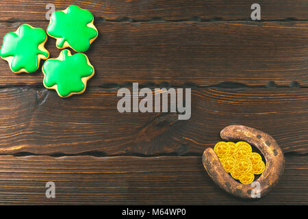 Patrick's day sfondo con gingerbread trifoglio e a ferro di cavallo con monete d oro su sfondo di legno Foto Stock