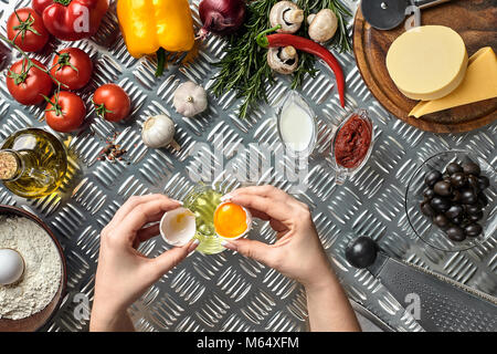 Set di ingredienti per la pizza e il panettiere mano smash uova sul tavolo in metallo. Funghi, pomodori, formaggio, cipolla, olio, pepe, sale, l'uovo, la grattugia in metallo b Foto Stock