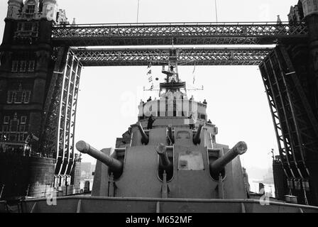 Le pistole in mostra sulla HMS Belfast come lei passa attraverso il Tower Bridge sul suo modo alla sua finale di ormeggio, appena sopra il ponte. Foto Stock