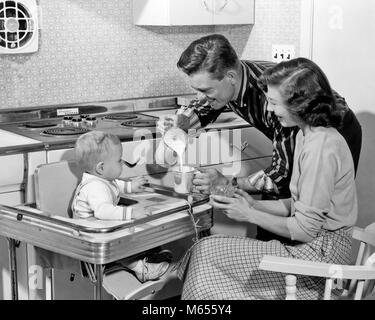 Degli anni Cinquanta padre versando il latte nella tazza PER FIGLIO IN ALTA SEDIA CON MADRE SEDUTI A LATO - b1906 HAR001 HARS CUP NEONATI MOM STRESS ABBIGLIAMENTO nostalgico versando coppia suburbana elegante madri vecchio tempo futuro OLD FASHION 1 che alimenta i capretti di sicurezza stile TEAMWORK CAUCASIAN LIETA GIOIA LIFESTYLE celebrazione femmine coniuge sposato mariti salubrità HOME vita seduti spazio copia di metà lunghezza LADIES FITNESS fisico cura le coppie in interni fiducia nostalgia padri convivere 1-2 anni 25-30 anni successo mogli felicità WELLNESS mamme papà emozione progressi orgoglio competente sorride gioiosa Foto Stock