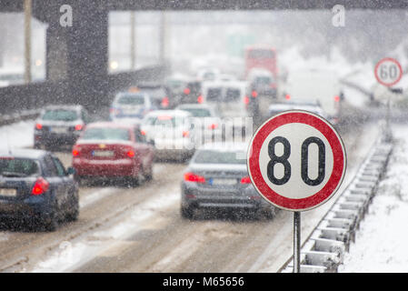 In inverno il traffico durante la tempesta di neve con scarsa visibilità. Segnale di limite di velocità con un traffico in background su una strada sdrucciolevole coperto con sn Foto Stock