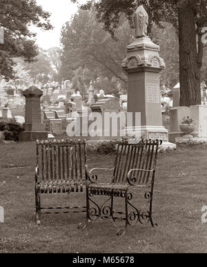 Anni Settanta due vuoto RUSTY sedie in ferro battuto insieme su erba nel Cimitero Cimitero - c11002 HAR001 HARS ESCAPE GRAVE SIMBOLICO MEMORIALI ASSENTE BATTUTO B&W in bianco e nero dei cimiteri cimitero DIE metallo ferroso tombe monumenti cimiteri vecchio arrugginito relazioni gli oggetti contrassegnati per la rimozione definitiva Foto Stock