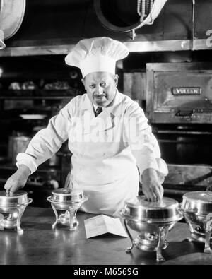 1920s 1930 GRAVI CHEF FRANCESE IN CUCINA CON piccolo argento Piatti sfregamento guardando la fotocamera - c3660 HAR001 HARS a metà lunghezza interni di carattere professione dirigenti nostalgia di mezza età uomo di mezza età biancheria contatto visivo 40-45 anni 45-50 ANNI DI OCCUPAZIONE CARRIERE CARATTERI LEADERSHIP borchie orgoglio la creatività dei cuochi maschi dirigenti sous-chef TOQUE B&W in bianco e nero di etnia caucasica lo sfregamento dello chef de cuisine chef de partie PREPARAZIONE ALIMENTARE GIACCA BIANCO guardando la telecamera di occupazioni in vecchio stile persone cuoco professionista ristoratore Foto Stock