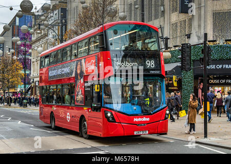 Una donna aspetta di attraversare un passaggio pedonale, come un autobus n. 98 Londra a Holborn fa la strada lungo Oxford St a Londra, Regno Unito Foto Stock