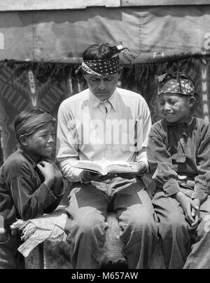 1930s Native American Indian NAVAJO uomo padre libro di lettura per due ragazzi sorridenti figli - MI1105 HAR001 HARS capretti informazioni di comunicazione figli lieta gioia LIFESTYLE FRATELLI PARENTING CASA RURALE VITA spazio copia amicizia a mezza lunghezza indiani navajo fratelli americana americani famiglie nostalgia padri di mezza età NORD AMERICA STARE INSIEME uomo di mezza età 10-12 anni 35-40 anni 40-45 anni 7-9 anni NORTH AMERICAN PRETEEN BOY FELICITÀ ALLEGRO DADS conoscenza i gemelli sorride gioiosa Native American piccolo gruppo di persone a sud-ovest i ragazzi maschi pre-teen BOY B&W IN BIANCO E NERO indigeni Foto Stock