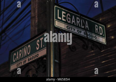 Orientati perpendicolarmente il nome della strada segni all'Cariño-Legarda bivio scarsamente illuminata di notte dalle luci della strada intorno a. Baguio-Bengu Foto Stock