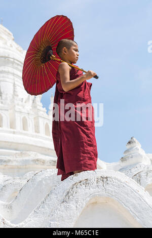 Giovane debuttante monaco buddista holding ombrellone a Pagoda Myatheindan (noto anche come Pagoda Hsinbyume), Mingun, Myanmar (Birmania), l'Asia in febbraio Foto Stock