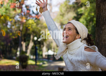 Entusiastico amore medio anziana signora con le braccia aperte fissando le foglie marrone in aria a park durante la stagione autunnale Foto Stock