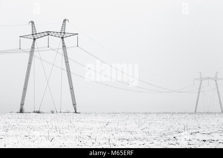 Alta tensione potenza elettrica linee in una nebbiosa invernale paesaggio, foto in bianco e nero. Foto Stock