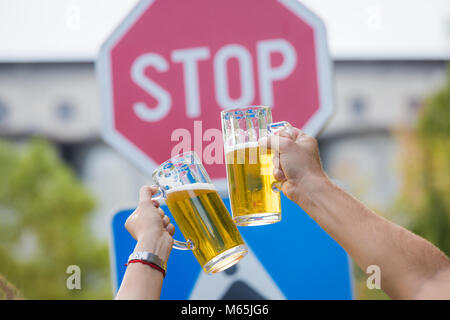 Chiudere fino a due mani boccali di birra di fronte a fermare un cartello stradale. L'abuso di alcool e la prevenzione dell'alcolismo. Non bere e guidare il concetto Foto Stock