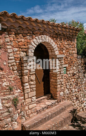 Vista della porta di legno e la parete e arco in pietra sotto un sole cielo blu, al Roussillon Villaggio. Situato nella regione della Provenza, Francia sudorientale. Foto Stock