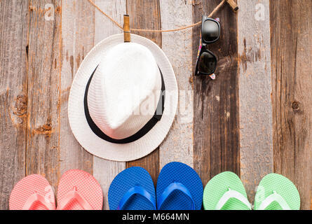 Luminose flip flop sandali. Cappello e occhiali da sole appeso su una linea con uno sfondo di legno Foto Stock
