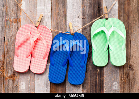 Rosa, il blu e il verde flip flop sandali. Flip-flop appeso su una linea con uno sfondo di legno Foto Stock