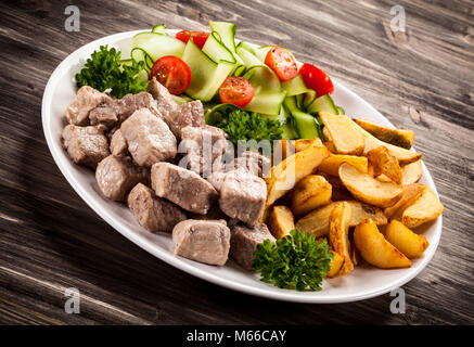 Grigliate di carne con patate fritte e verdure sul tavolo di legno Foto Stock