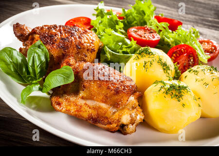 Arrostire le cosce di pollo con patate lesse e insalata di verdure sul tavolo di legno Foto Stock