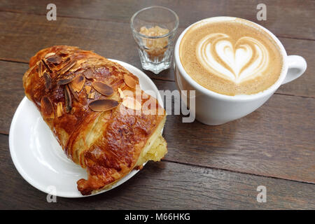 Colazione perfetta combinazione: tazza di cappuccino e freschi di forno croissant alle mandorle. Foto Stock