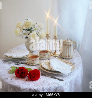 Tabella impostata per il servizio da tè per 2 con candele e bouquet di fiori - kf38501 MAT002 HARS rose bianche Foto Stock