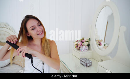 Femmina affascinante allinea i capelli utilizzando arricciacapelli e capelli, seduti su una sedia Foto Stock