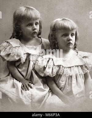 1890s ritratto giro del 20esimo secolo due gemelle sorelle indossando abiti identici e che mostra imbronciato triste le espressioni del viso - o4472 HAR001 HARS NOSTALGIA TRISTEZZA STARE INSIEME 1-2 anni 3-4 anni MATCHING stesso giro del 20esimo secolo 1890s i gemelli Collegamento anonimo look-alike duplicare emozione emozioni emotivo novellame si assomigliano B&W in bianco e nero di etnia caucasica clone imbronciato di vecchio stile Foto Stock