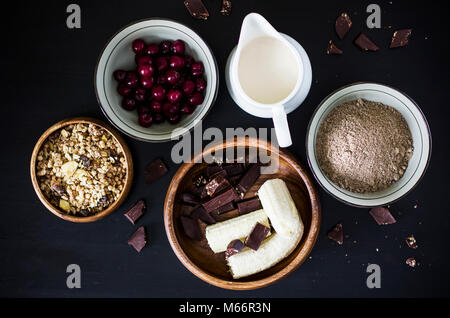 Muffin Ingredienti: latte, muesli, congelati ciliegia, farina di lino, banana e cioccolato su sfondo nero Foto Stock