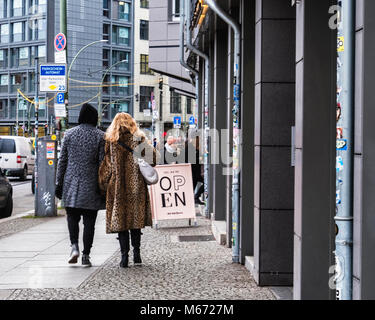 Moda giovane coppia spotted animale cappotti di pelliccia camminando per strada urbana nel quartiere Mitte di Berlino Foto Stock