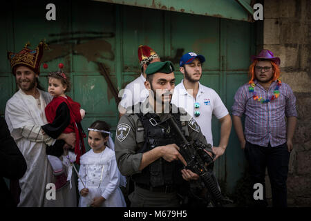 Dpatop - un soldato israeliano sta di guardia come costume i coloni israeliani prendere parte alla parata segna la festa ebraica di Purim in divisa in Cisgiordania città di Hebron, 01 marzo 2018. La carnevalesca Purim holiday è celebrata con sfilate in costume e parti per commemorare la liberazione del popolo ebraico dalla un complotto per sterminarli nell'antico impero persiano 2.500 anni fa, come registrato nel libro biblico di Ester. Foto: Ilia Yefimovich/dpa Foto Stock