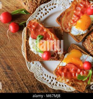 La prima colazione , bacon croccante, uova fritte e pane. Panini sulla piastra bianca. Tavolo rustico . Vista superiore Foto Stock