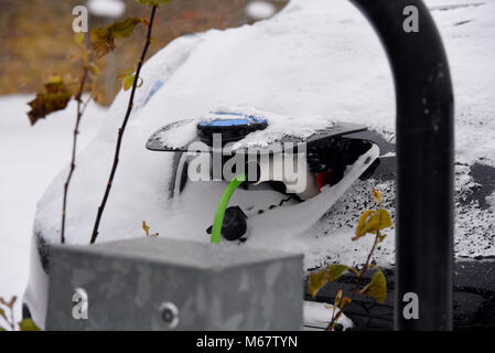 Auto elettrica punto di carica con la neve soffiata all'interno della presa per auto e il tappo ad esagono incassato l'apertura della porta. Durante la bestia da est meteo fenomeno. Foto Stock