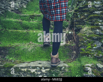 Una giovane donna che indossa scarpe da trekking e un mantello è a piedi il muschio coperto passi nella natura Foto Stock