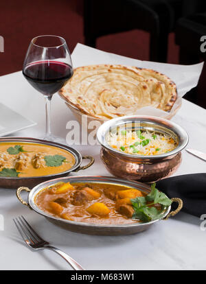 Il curry indiano alimento spalmato su una cena elegante tavolo con riso, laccha paratha, agnello aam wala, zafferano malai kofta, vino rosso. Foto Stock