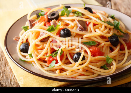 Spaghetti alla putanesca con acciughe, pomodori, aglio e olive nere close-up su una piastra orizzontale. Foto Stock