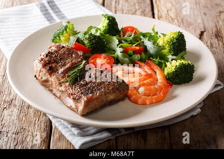 Deliziose grigliate di carne di manzo con gamberi e broccoli, pomodori, rucola closeup su una piastra su un tavolo. Surf and Turf orizzontale. Foto Stock