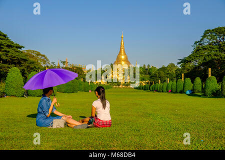 Due giovani donne sono seduti su un prato di fronte al golden Shwedagon pagoda, il più sacro pagoda di Myanmar, situato su una collina nel centro di Foto Stock