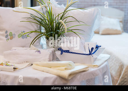 White set di cuscini con ricami curato nei pressi di biancheria da letto e la pianta verde in negozio per uso domestico Foto Stock