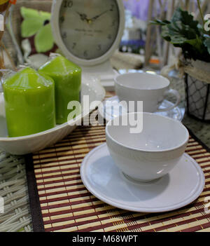 Still Life - bianco tazze da caffè disposto su una tavola con vintage orologio bianco e verde di due candele decorative Foto Stock