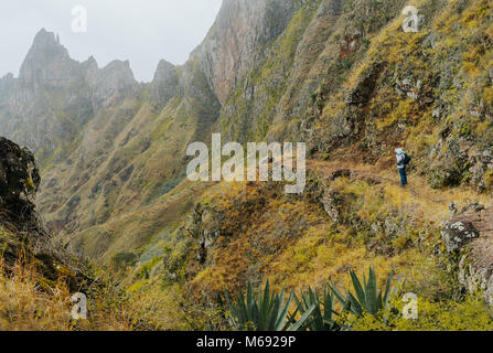 Viaggiatore con telecamera di fronte alla monumentale cresta di montagna e il burrone sul sentiero acciottolato a valle Xo-Xo. Santo Antao Isola, Capo Verde Foto Stock